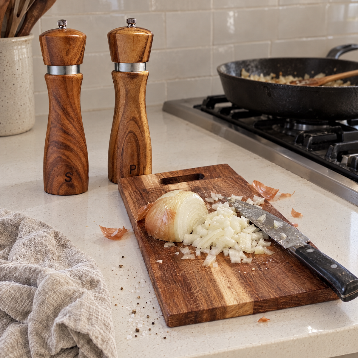 Acacia salt and pepper grinders next to an acacia cutting board with a chopped onion